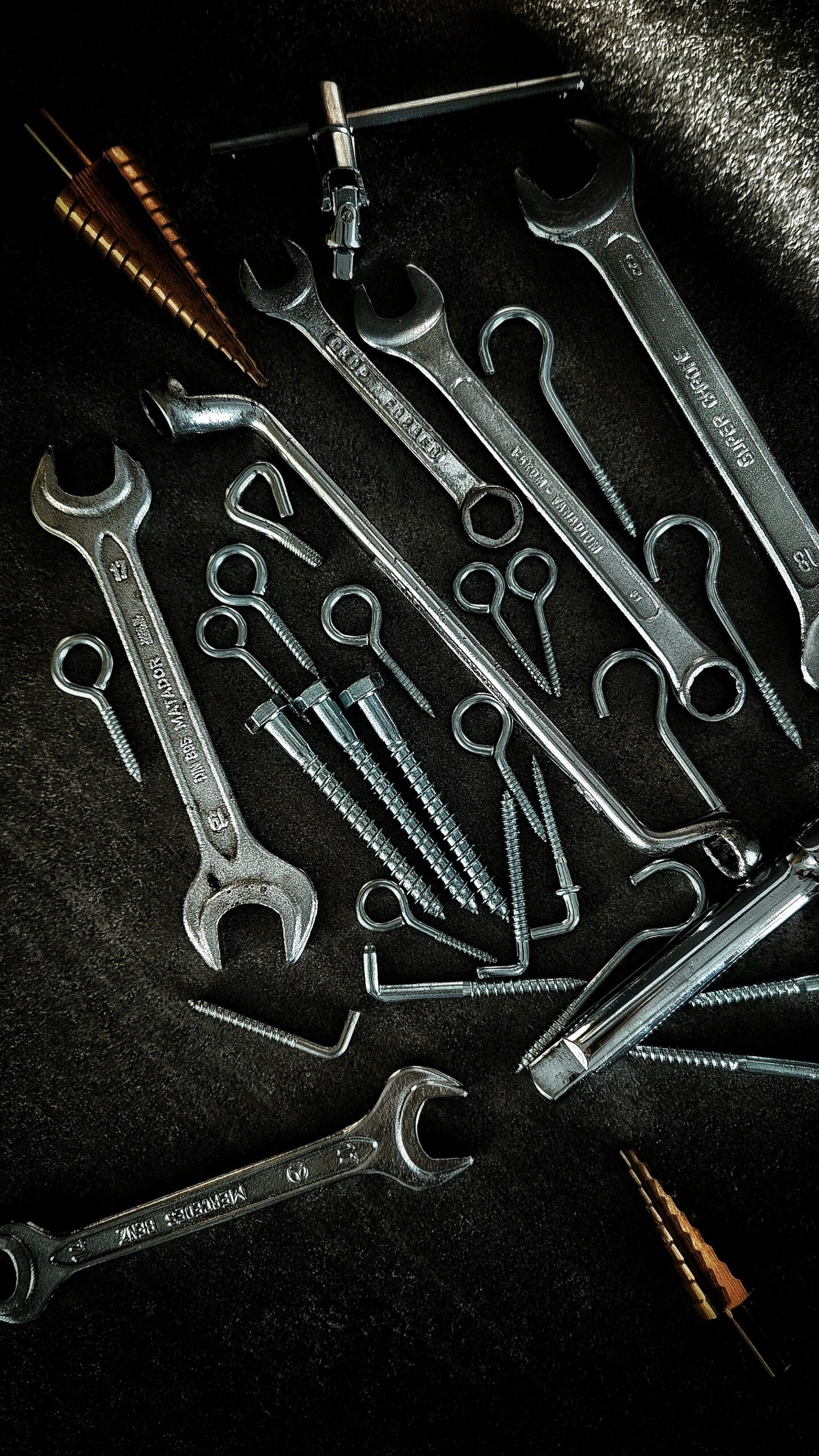 Various hand tools and hardware accessories, including wrenches, hooks, anchors, and screws, displayed on a dark textured surface.